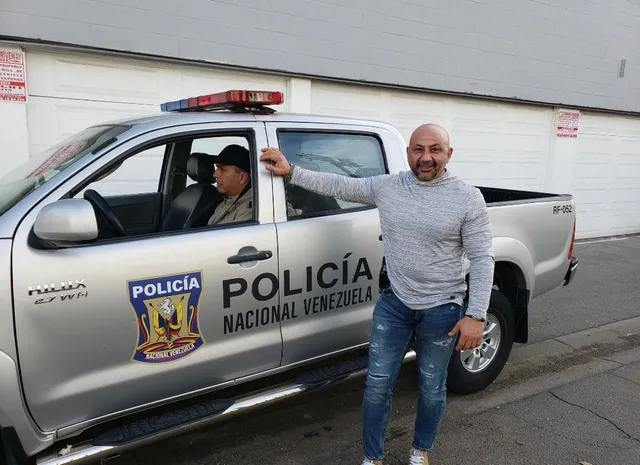 A man is standing in front of a silver police truck