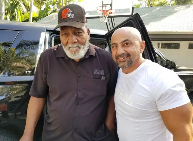 Two men are posing for a picture in front of a car